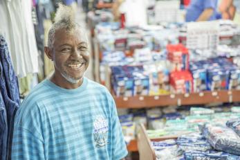 Puerto Rican man stands amidst commercial stalls, smiling.