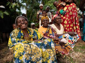 Congolese community members sitting outside in colorful clothing, smiling.