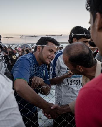 Iraqi civilians displaced after conflict shaking hands over a fence