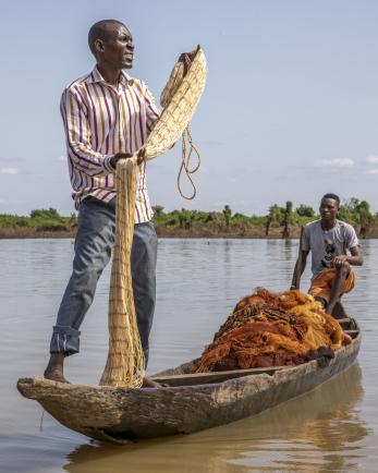 An adult manipulates a fishing net while standing on a boat in a river in Nigeria.