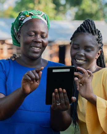 Two women consulting a tablet device and smiling.