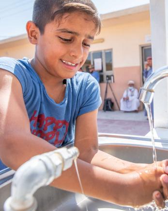 A young person washing their hands in an outdoor sink.