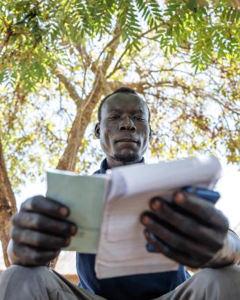 Ugandan man sits under a tree reviewing notes.
