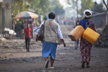 Mercy Corps officer Silvie, left, walks alongside Noella as she heads to a Mercy Corps pump to collect water.