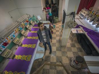 Man standing between rows of purple fabric and sewing machines