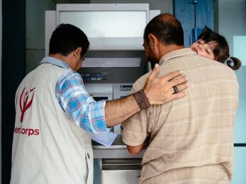 Mercy corps team member helping a father (holding his daughter) to use an atm