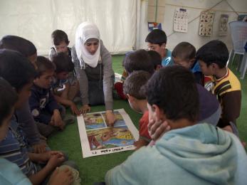 Children gathered around a woman who is leading the group in an activity