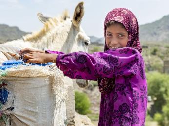 Girl in yemen next to animal carrying water