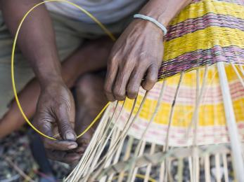 Hands weaving a yellow basket