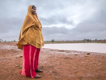 Woman dressed in dark yellow and red, standing near a body of water