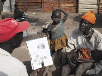 Two men talking to one another, with a child standing between them. one man is holding a baby.