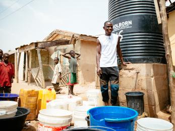 Nigerian man in front of water cistern and home.