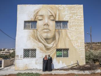 Two woman in front of a building with a large mural painted on it.