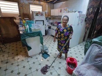 Carmen stands in her kitchen with a mop and bucket