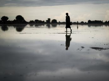 Woman walking under cloudy sky with silhouette reflected on wet ground