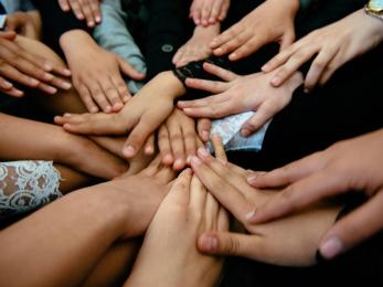 Several hands reaching to the center