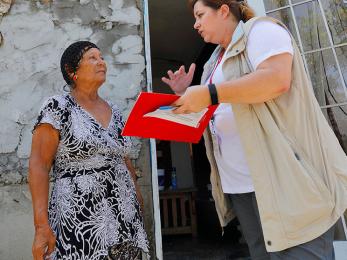 A mercy corps team member holding a folder, paper and pen speaks to a woman in puerto rico