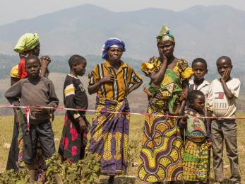 Woman and children standing behind a strip of red and white tape in drc