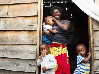 Justine stands in the doorway of her small wooden home, which is the only source of light for the tiny space built on lava rock. she and her family are grateful for the mercy corps tap stand across the street that brings clean water close to their home. photo: liz hummer/mercy corps