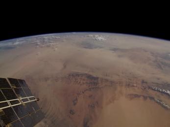 A photo showing a portion of a satellite and the curve of the earth, with the brown sahara making up the majority of the land shown