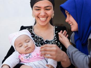 Two smiling women. the woman on the left is holding a sleeping baby.
