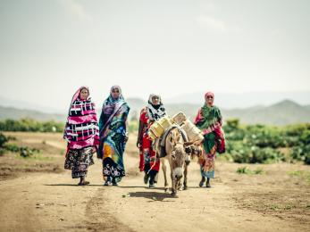 Four women in ethiopia wearing bright colors and walking behind a donkey