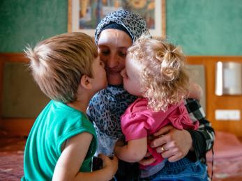 A woman receives kisses on her cheeks from a young boy and girl as she holds them tight