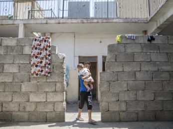 A boy in a cinderblock doorway holding a baby