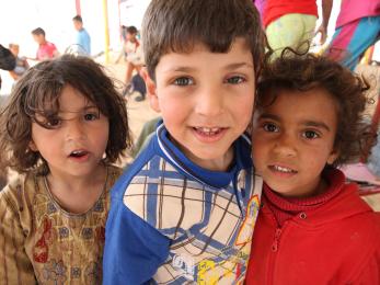 Three young children smile at zaatari camp.