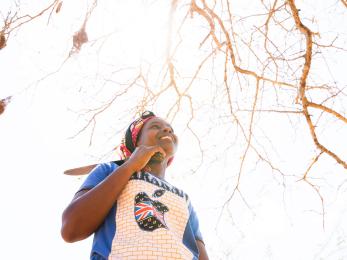 A woman farmer in kenya pictured with bare tree branches above her