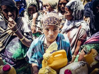 Ethiopian holding water can and looking at camera
