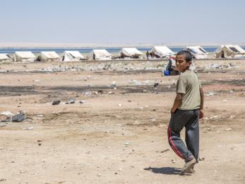 A boy walks toward a row of white tents in a dry, desert landscape