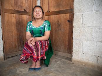 Young woman sitting in corner of room, in front of two doors.