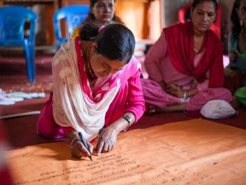 Woman writing on large sheet of paper with group behind.