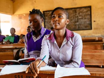 A high school student in nigeria leans forward in their seat inside a classroom with students. 