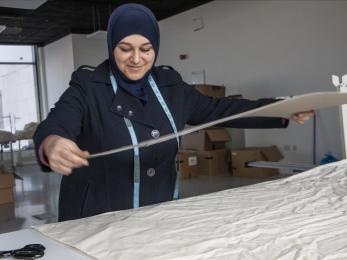 Jordanian woman measures textiles in workspace.