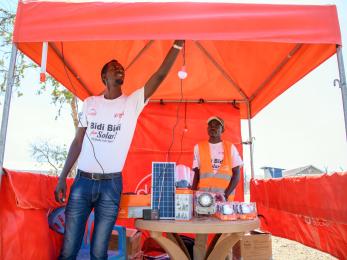 A person hangs a light in a temporary pop-up canopy filled with solar electrical equipment. 