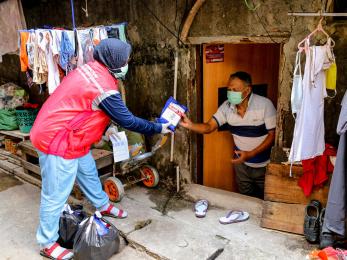 A mercy corps staff team member hands someone a hygiene kit during a door to door community outreach event in jakarta province.