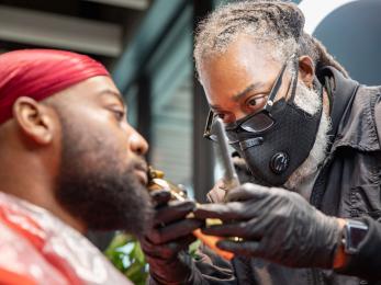 A barber trims the beard of a customer. 