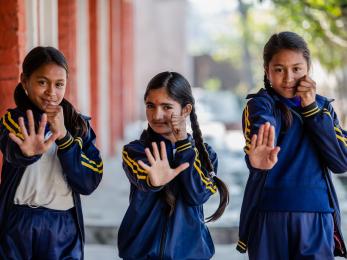 Three nepalese girls pose with hands out in front of them.