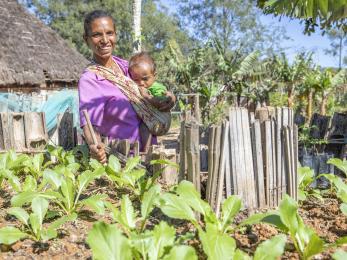Timor leste woman in vegetable garden with child.