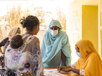 A person carrying a child speaking with two people at a table completing forms. 