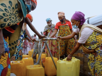 A group of people filling jerry cans at a water station.