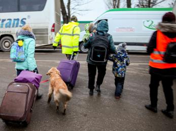 Emergency aid workers escorting women, children, and a dog to vehicles.