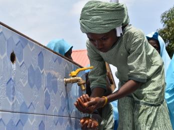 A young person washing their hands from a spigot.