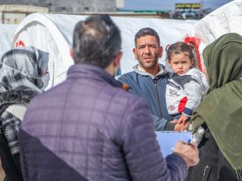 Adults with children speaking with aid workers about receiving emergency supplies.