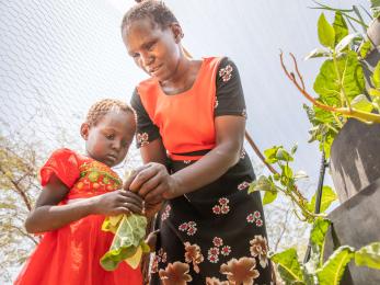 A mother teaching her daughter to pick vegetables from their garden.