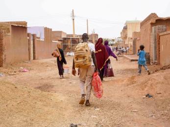 Sudanese community members walk down local street with baggage.