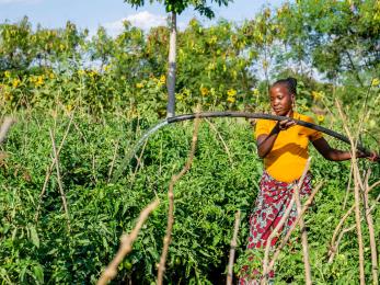 Tanzanian woman working with irrigation equipment in agricultural setting.