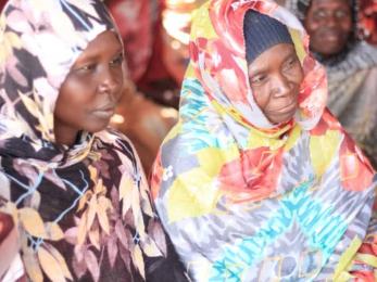 Two people sitting together listening to someone speak at a gathering..